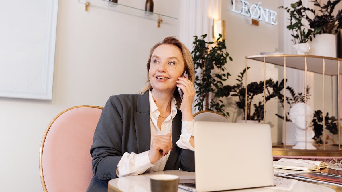 Businesswoman in office, speaking on phone, smiling, with laptop.